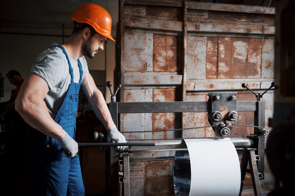 portrait of a young worker in a hard hat at a large metalworking plant. the engineer serves the machines and manufactures parts for gas equipment
